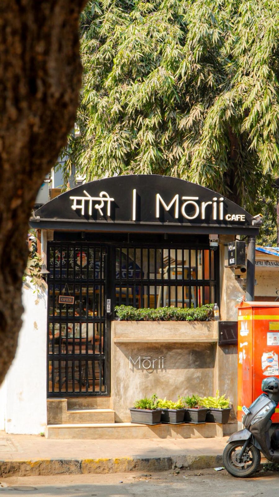 Morii's black café sign and gated street entrance beneath trees in Mount Mary, Bandra.